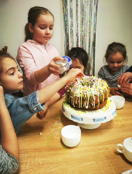4 dzieci, dziewczynki, dekorują stojącą na stole babkę wielkanocną