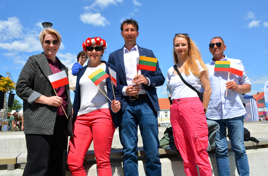 Pięć osób, 3 kobiety i dwóch mężczyzn stoi obok siebie, w rękach trzymają małe flagi Litwy i Polski.