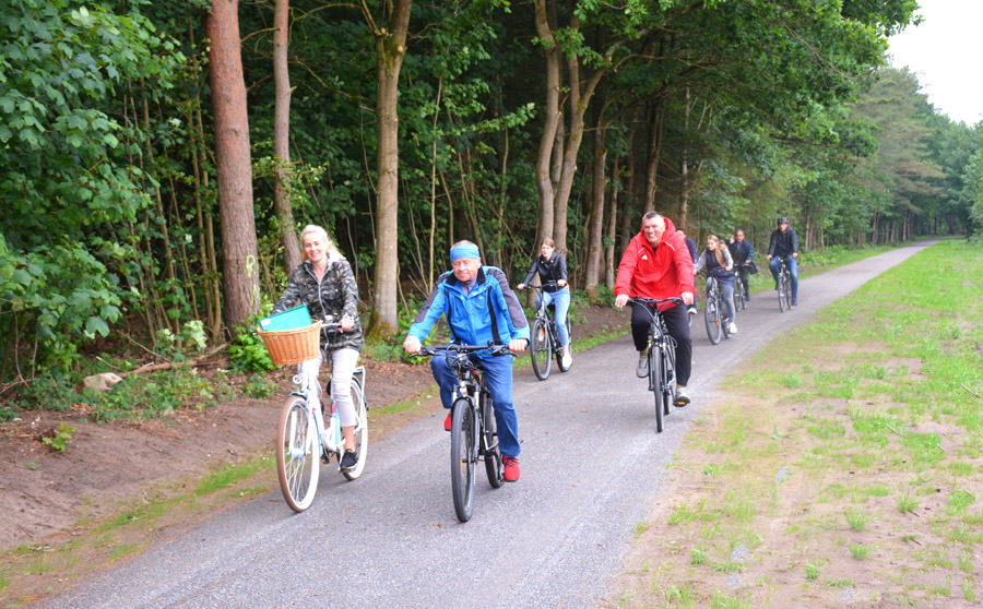 Grupa ludzi jedzie rowerami ścieżką rowerową położoną w lesie