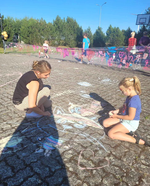 Kobieta i młoda dziewczynka siedzą na boisku z kostki i malują kredą.